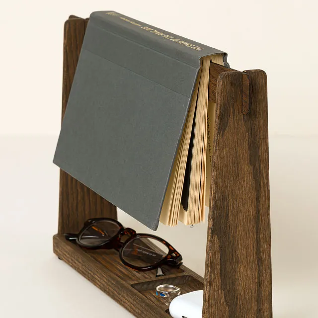 A wooden bookmark stand with a grey book on top and glasses and accessories in the bottom tray